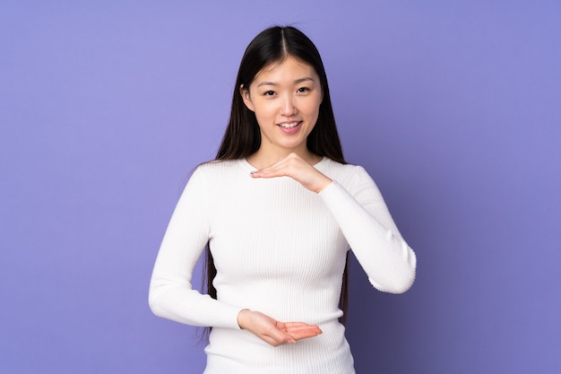 Junge asiatische Frau auf lila Wand, die Leerzeichen imaginär auf der Handfläche hält