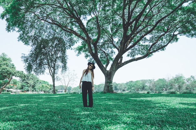 Junge asiatische Frau des Porträts mit der Hippie-Art, die unter dem großen Baum im Garten steht