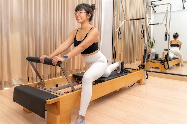 Junge asiatische Frau, die an Pilates-Reformer-Maschine während ihres Gesundheitsübungstrainings arbeitet