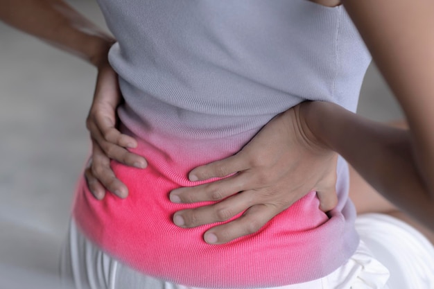 Junge asiatische Frau, die auf dem Bett sitzt und unter Rückenschmerzen leidet Erwachsene Frau hält ihren unteren Rücken und leidet unter chronischen Rückenschmerzen Gesundheitsversorgung und medizinisches Konzept