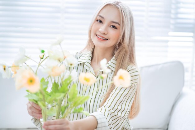 Junge asiatische Frau, die Blumen im Wohnzimmer arrangiert