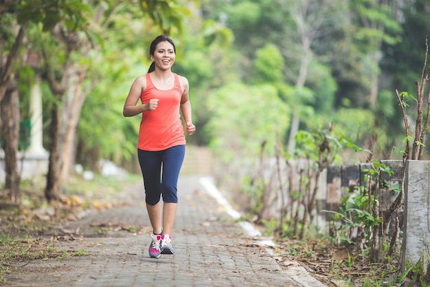 Junge asiatische Frau, die Übung im Freien in einem Park macht, joggend