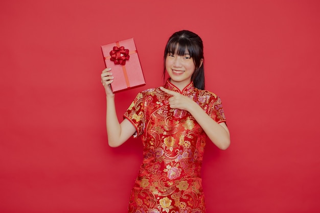 Junge asiatische Frau, die cheongsam Kleid trägt und Geschenk hält