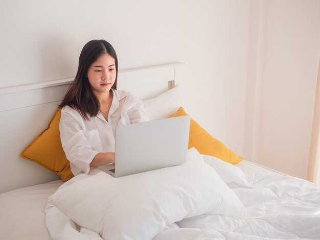 Junge asiatische Frau, die Computer im Schlafzimmer verwendet