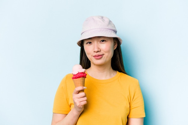 Junge asiatische Frau, die ein Eis isst, isoliert auf blauem Hintergrund