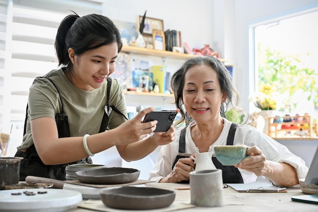 Junge asiatische Frau, die ein Foto einer keramischen Kaffeetasse in den Händen der gealterten Frau macht