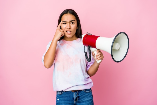 Junge asiatische Frau, die ein Megaphon lokalisiert auf rosa Wand hält, die eine Enttäuschungsgeste mit Zeigefinger zeigt.