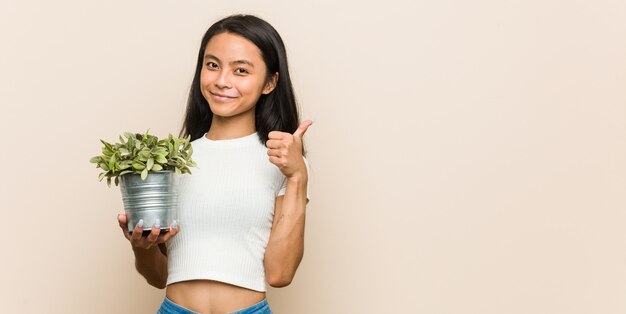 Junge asiatische Frau, die eine Anlage lächelt und angehoben Daumen hält