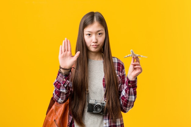 Junge asiatische Frau, die eine Flugzeugikone steht mit der ausgestreckten Hand zeigt das Stoppschild und verhindert Sie hält.