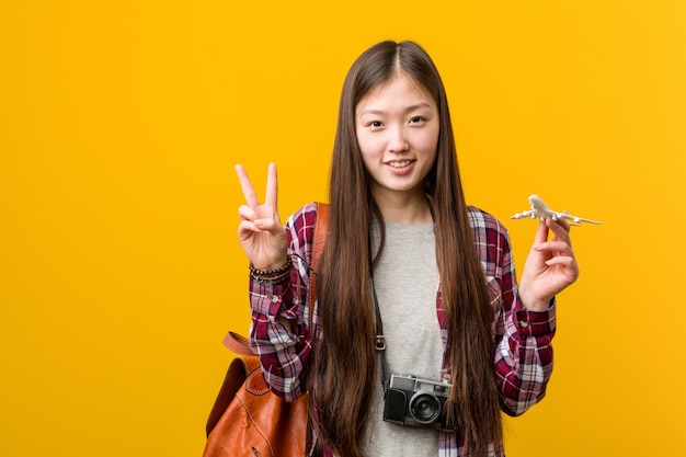 Junge asiatische Frau, die eine Flugzeugikone zeigt Nummer zwei mit den Fingern hält.