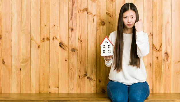 Junge asiatische Frau, die eine Hausikone zeigt Faust zur Kamera, aggressiver Gesichtsausdruck hält.