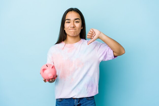 Junge asiatische Frau, die eine rosa Bank über isolierter Wand hält, die eine Abneigungsgeste zeigt, Daumen nach unten. Uneinigkeit Konzept.