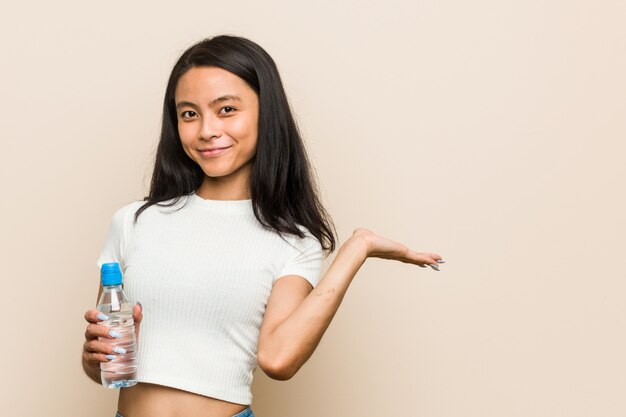 Junge asiatische Frau, die eine Wasserflasche hält eine andere Hand auf Taille hält.