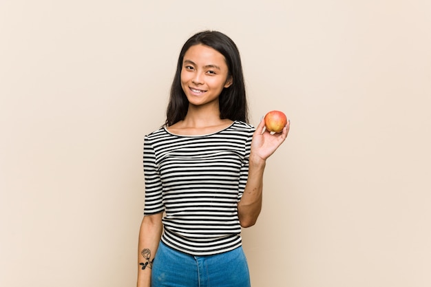Junge asiatische Frau, die einen Apfel glücklich, lächelnd und nett hält.
