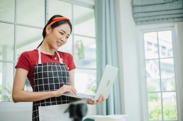 Junge asiatische Frau, die einen Computer benutzt, um in ihrer Küche zu kochen