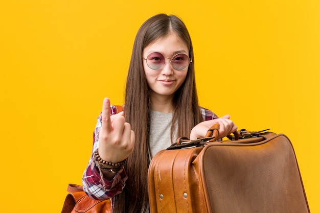 Junge asiatische Frau, die einen Koffer zeigt mit dem Finger auf Sie hält, als ob Einladung näher kommen.