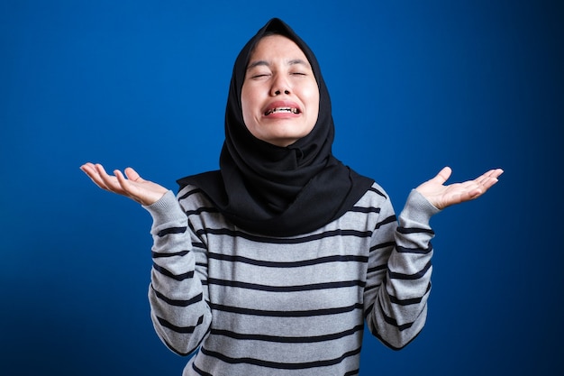 Junge asiatische Frau, die einen traditionellen islamischen Hijab-Schal trägt und denkt, müde und gelangweilt mit Depressionsproblemen vor blauem Hintergrund