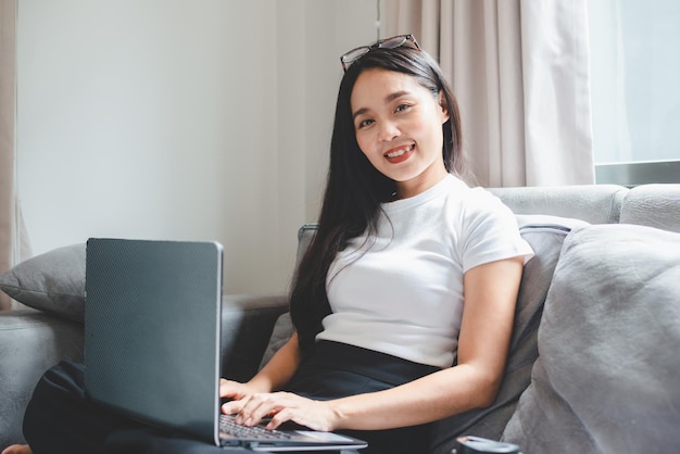 Junge asiatische Frau, die freiberuflich tätig ist, arbeitet am Laptop zu Hause und arbeitet von zu Hause aus