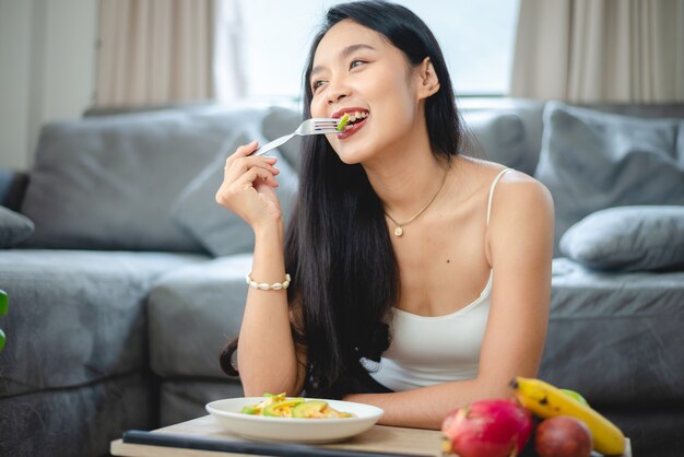 Junge asiatische Frau, die gesundes Gemüse im Lebensstil zu Hause hält, weibliche schöne vegetarische Person, die Diätnahrung macht, isst Salatmahlzeit, die Leute lächeln glücklich, gesundes Lebensmittelkonzept