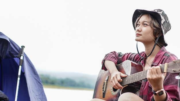 Junge asiatische Frau, die Gitarre am Camping spielt