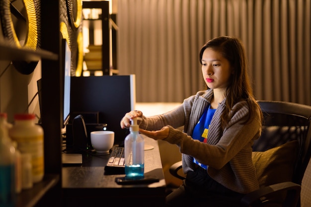 Junge asiatische Frau, die Händedesinfektionsmittel während der Arbeit von zu Hause in der Nacht verwendet