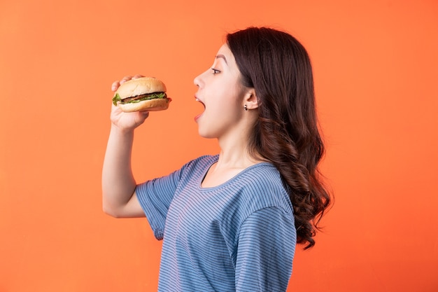 Junge asiatische Frau, die Hamburger auf Orange isst