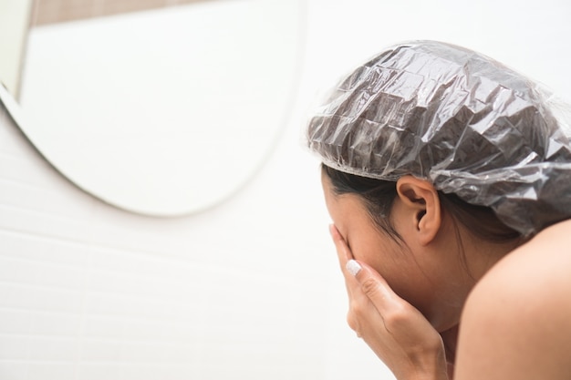 Junge asiatische Frau, die ihr Gesicht vor Dusche im Badezimmer wäscht.