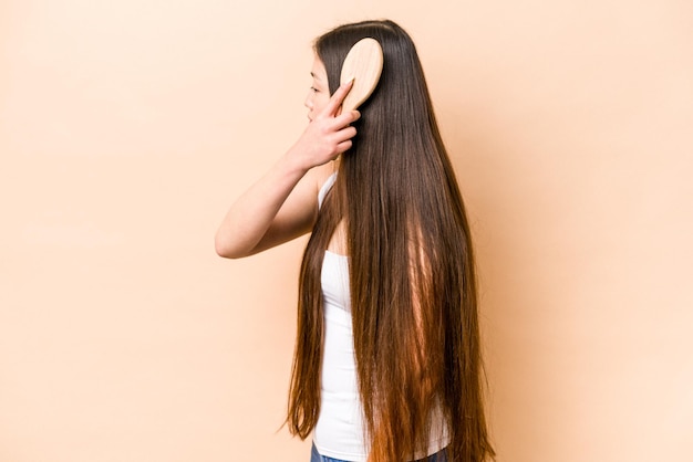 Junge asiatische Frau, die ihr Haar einzeln auf beigem Hintergrund kämmt
