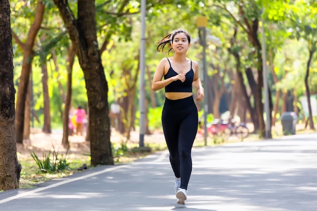 Junge asiatische Frau, die im Park auf Straße in Sportbekleidung läuft.