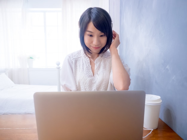 Junge asiatische Frau, die Kopfhörer vor Laptop hört