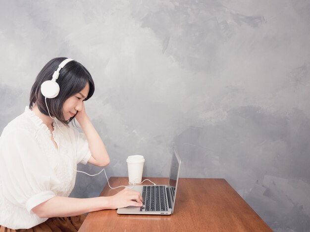 Junge asiatische Frau, die Kopfhörer vor Laptop hört