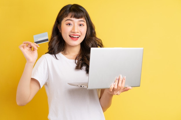 Junge asiatische Frau, die Laptop auf Gelb hält