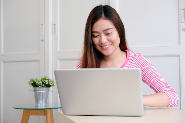 Junge asiatische Frau, die Laptop-Computer verwendet und mit Glück lächelt