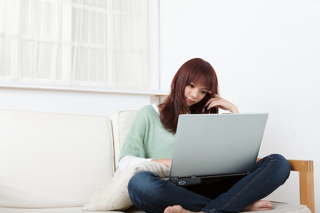 Junge asiatische Frau, die Laptop zu Hause auf Sofa verwendet.