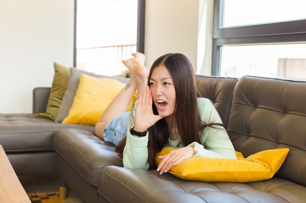 Junge asiatische Frau, die laut und wütend schreit, um Platz auf der Seite mit Hand neben Mund zu kopieren