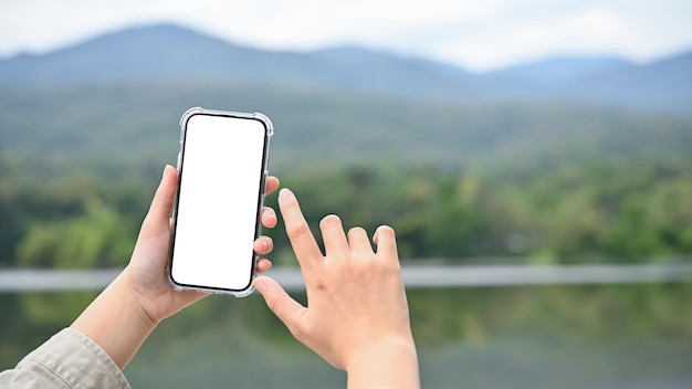 Junge asiatische Frau, die mit ihrem modernen Smartphone ein Foto von See und Berg macht