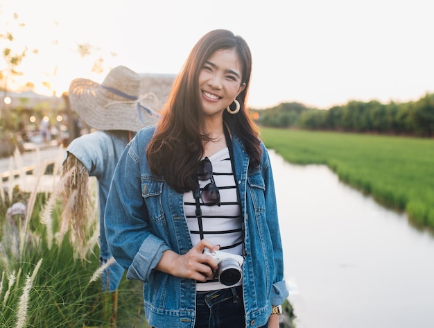 Junge asiatische Frau, die mit Kamera lächelt. Mädchen, das an der schönen Natur mit Sonnenuntergang genießt.