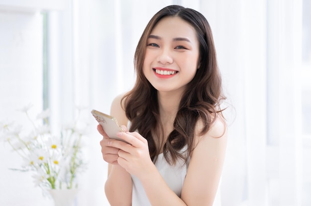 Junge asiatische Frau, die morgens zu Hause Smartphone benutzt