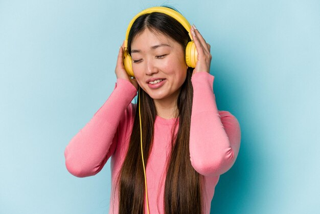 Junge asiatische Frau, die Musik isoliert auf blauem Hintergrund hört