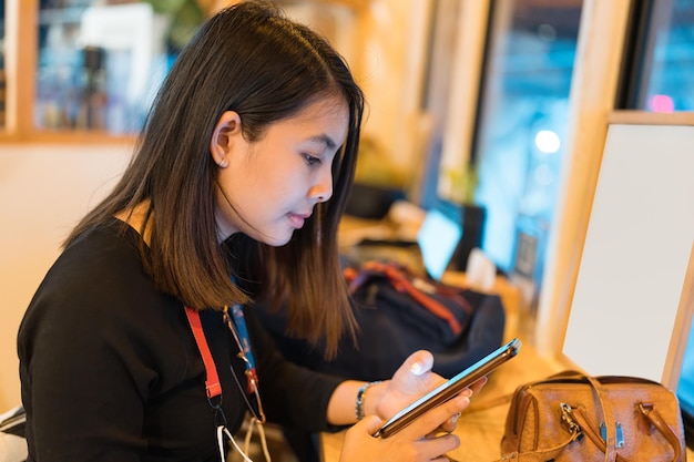 Junge asiatische Frau, die nachts im Café an der Holztheke sitzt und ein Smartphone benutzt