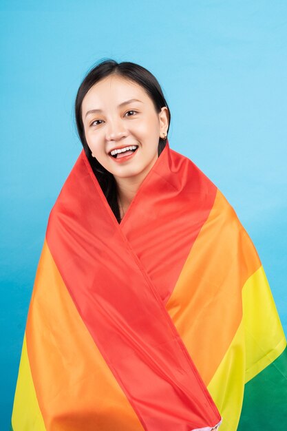 Junge asiatische Frau, die Regenbogenfahne hält, um LGBTQ + Gemeinschaft auf Blau zu unterstützen