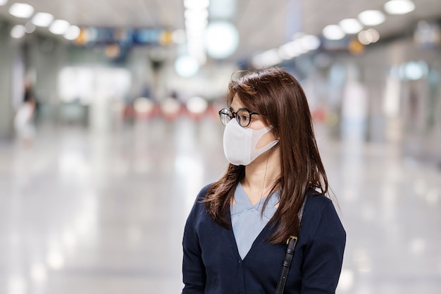 Junge asiatische Frau, die Schutzmaske gegen neuartiges Coronavirus oder Corona-Virus-Krankheit (Covid-19) am Flughafen trägt