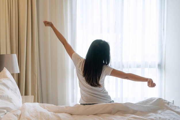 Junge asiatische frau, die sich nach dem aufwachen mit sonnenlicht morgens im schlafzimmer zu hause oder im hotel ausdehnt closeup copy spacex9