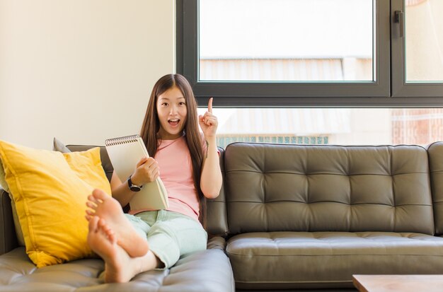 Junge asiatische Frau, die sich wie ein glückliches und aufgeregtes Genie fühlt, nachdem sie eine Idee verwirklicht hat, fröhlich Finger hebend, eureka!