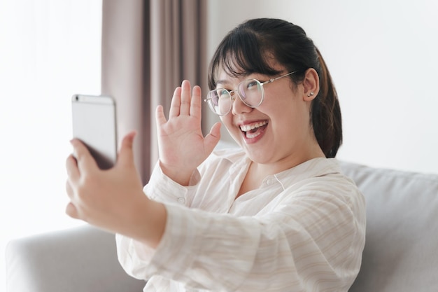 Junge asiatische Frau, die Smartphone für Online-Videokonferenzanrufe verwendet, winkt mit der Hand und macht Hallo-Gesten