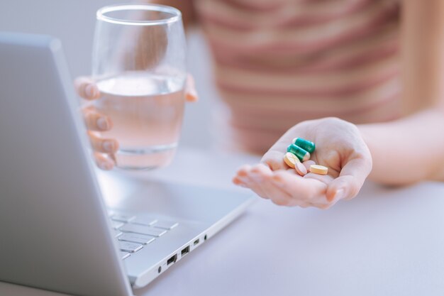 Junge asiatische Frau, die Tasse Wasser und Medizin in der Hand hält, um für Gebrauch vorzubereiten