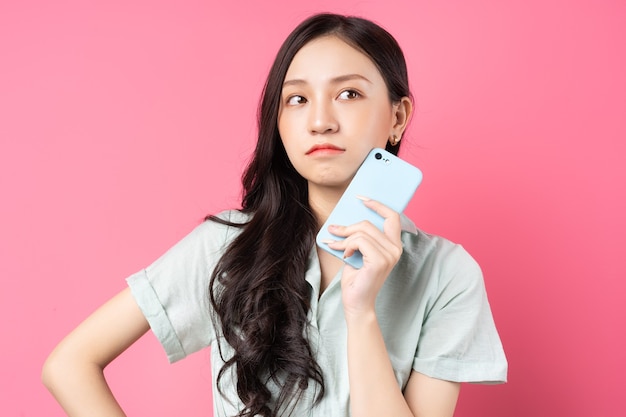 Junge asiatische Frau, die Telefon in ihrer Hand mit nachdenklichem Blick auf Rosa hält