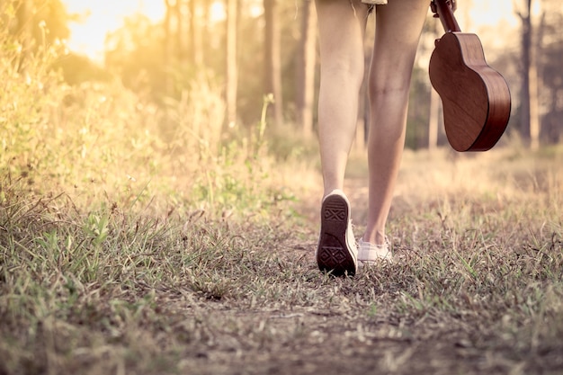 Junge asiatische Frau, die Ukulele hält und in den Park im Weinlesefarbton geht