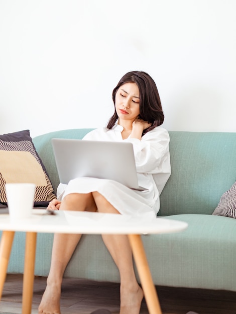 Junge asiatische Frau, die unter Schmerzen in der Schulter leidet, wenn sie einen Laptop benutzt