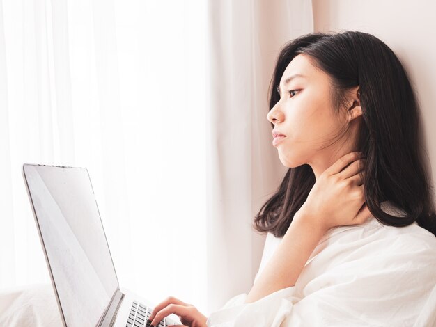 Junge asiatische Frau, die unter Schmerzen in der Schulter leidet, wenn sie einen Laptop benutzt